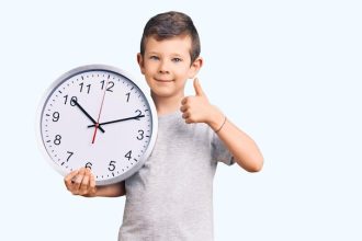 cute-blond-kid-holding-big-clock-smiling-happy-positive-thumb-up-doing-excellent-approval-sign_839833-8503