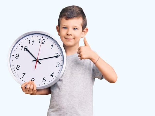 cute-blond-kid-holding-big-clock-smiling-happy-positive-thumb-up-doing-excellent-approval-sign_839833-8503